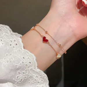 Detail of double-layer rose gold bracelet with red and mother-of-pearl heart charms