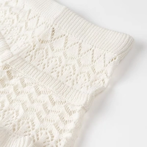 Close-up of white knitted fabric with intricate hollow geometric patterns and soft texture