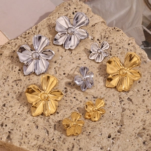 Detail of flower stud earrings in gold and silver finishes on natural stone surface
