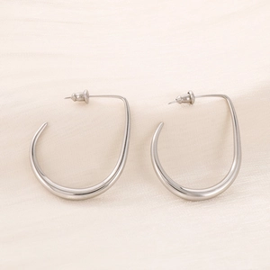 Close-up of silver U-shaped curved earrings on soft beige silk fabric background