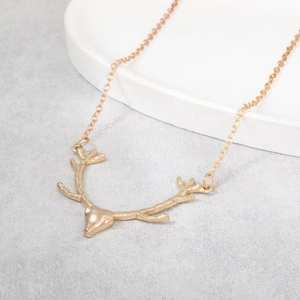 Detailed view of a golden deer antler pendant necklace displayed on a white ceramic plate