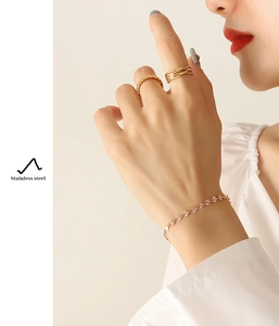 Close-up of gold stainless steel bracelet and rings set on model with floral textures