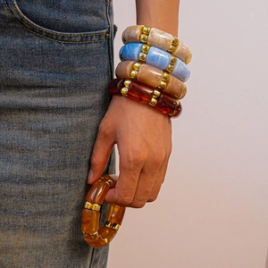 Close-up of stacked acrylic geometric beaded bracelets in amber and blue on a wrist