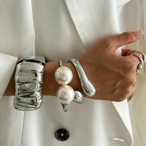 Chic silver pleated bracelets set with pearls and rings worn by woman in white blazer