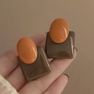 Close-up of vintage resin earrings featuring orange oval and brown square geometric design