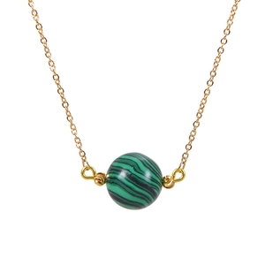 Macro detail of natural green malachite spherical pendant on a minimalist gold chain necklace