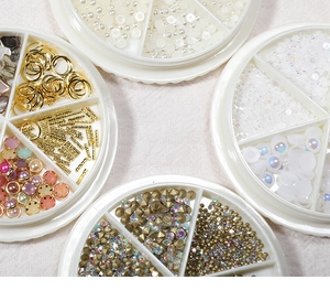 Flat lay of mixed nail art charms with pearls and metal studs in white sorting trays