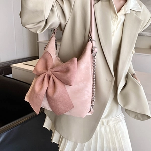 Pink suede hobo bag with large bow and chain strap worn by a model in a suit