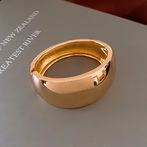 Polished gold wide-band open bangle bracelet with a sleek minimalist hinge design