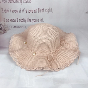 Macro detail of fine woven straw hat with wavy brim, pearl pendant, and ribbon bow