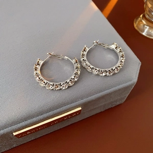 Close-up of silver hoop earrings with clear crystals on a grey velvet jewelry box