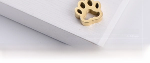 Detailed view of hollow dog paw pendant in polished gold finish on white wood