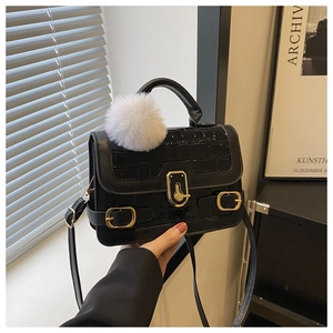 Details einer schwarzen Krokostruktur-Handtasche mit goldener Schließe und Plüschanhänger