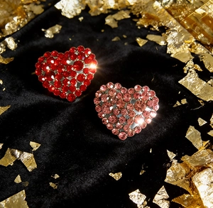 Detailed macro view of heart-shaped brooches with red and pink crystals on black velvet