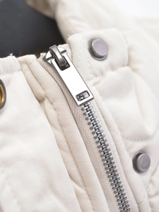 Detailed close-up of the silver metal zipper and snap buttons on a white puffer vest