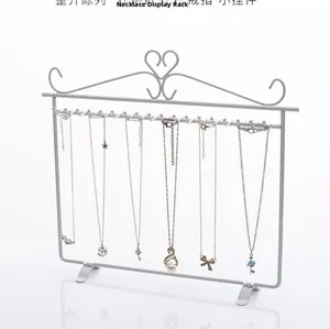 Wall-mounted white iron jewelry rack with heart detail and hooks for necklaces