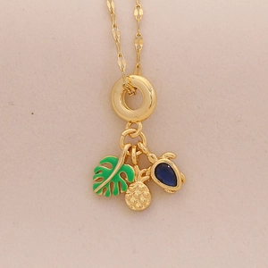 Detail of gold necklace featuring tropical palm leaf, pineapple, and blue turtle pendants