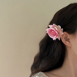 Pink fabric rose hair clip accessory shown on model with long wavy brown hair