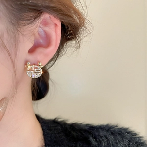 Detail of gold Fu character stud earrings with zircons shown on a female ear