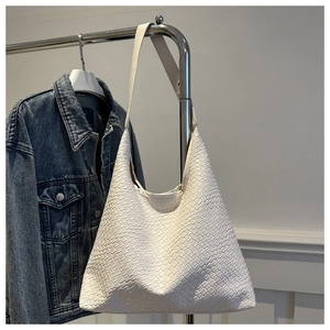 Detail of a white woven hobo bucket bag hanging against a denim jacket backdrop
