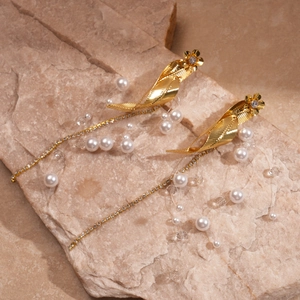 Vintage gold leaf and flower tassel earrings with white pearls on a natural stone surface