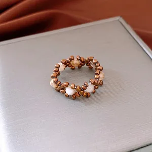 Vintage beaded stretch ring with bronze and white stones on a gray display case