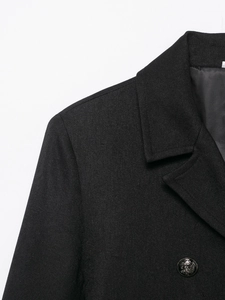 Detailed macro shot of a lion head embossed metal button on a black wool blend coat
