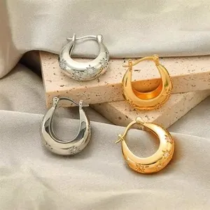 Detailed view of gold and silver chunky star-engraved hoop earrings on silk fabric