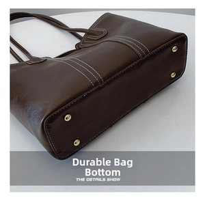 Detail of a dark brown leather tote bag with protective gold feet and contrast stitching