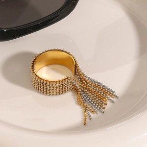 Golden stainless steel wide ring featuring beaded fringe tassels on a white ceramic plate
