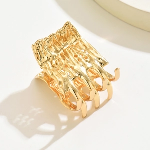 Close-up of golden metal hair claw with organic texture and curved comb teeth