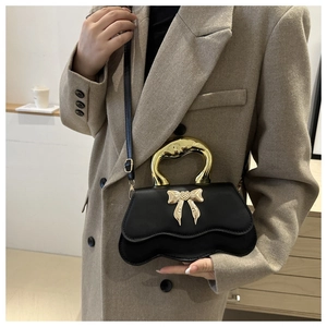 Detailed view of women's black leather bag with gold bow clasp and wavy metal handle