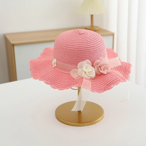 Detail of pink straw sun hat showing wavy brim, fabric flowers and delicate ribbon