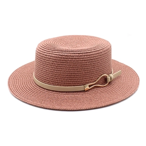Detail of pink straw boater hat featuring beige leather strap and gold metal buckle