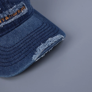 Macro detail of distressed blue denim baseball cap with gold letter embroidery texture.