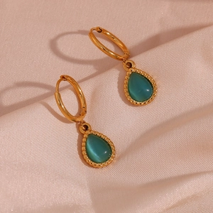Close-up of gold drop earrings with green cat-eye stone on soft pink silk fabric