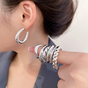 Detail view of silver drop earrings and geometric rings with high-polished metallic texture