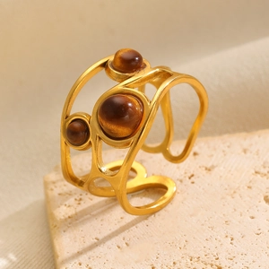 Detail of gold hollowed ring featuring tiger eye stones on a natural stone surface