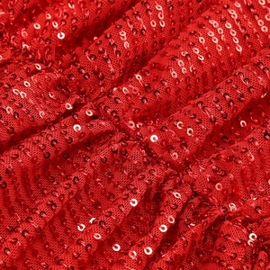 Macro shot of red sequin fabric detailing the natural folds and metallic luster of the dress