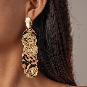 Macro view of gold hammered metal and leopard print circular drop earrings on a model