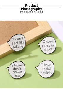 Detail shot of four white enamel pins featuring social anxiety phrases on a cork board