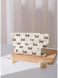 Minimalist cream cotton makeup bag with black bow patterns on a wooden tray