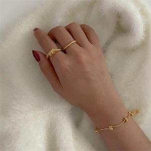 Three-piece gold jewelry set with twisted knot ring, wave ring, and delicate ball bracelet