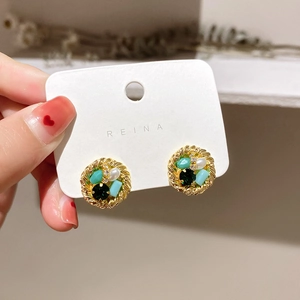 Detail of round gold woven stud earring with emerald stones and white pearls