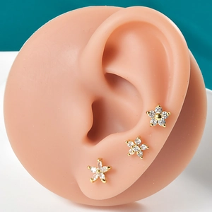 Close-up of golden flower stud earrings with white zircon stones on a model ear