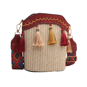 Detail of beige straw bucket bag with red PU trim, colorful strap and fringe tassels