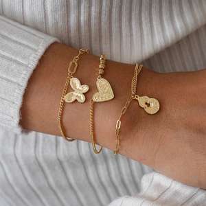 Three-piece gold layered bracelet set with butterfly and heart charms on a knit sweater