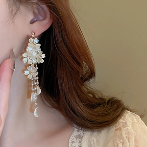 Close-up of elegant flower tassel earrings with pearls and gold chains on model