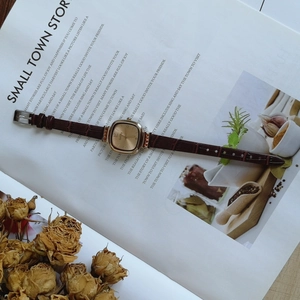 Flat lay of vintage square gold watch with brown leather strap on a magazine background