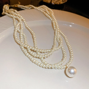 Detail of four-layer pearl necklace with a large round pendant on white ceramic plate